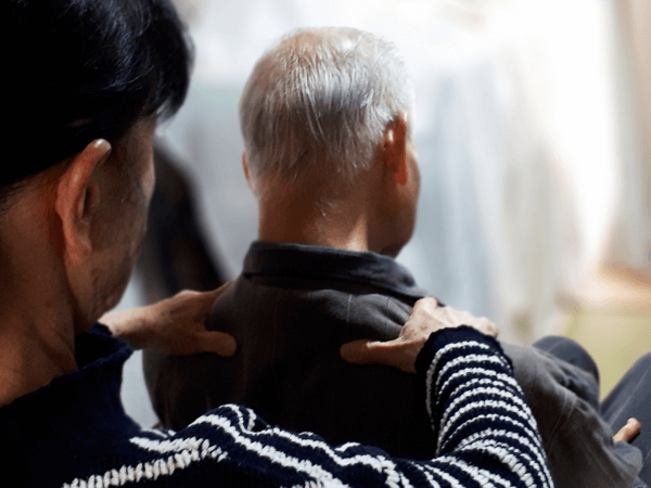 高齢の親と並んで座る中年の子供。家計の不安を感じさせる構図